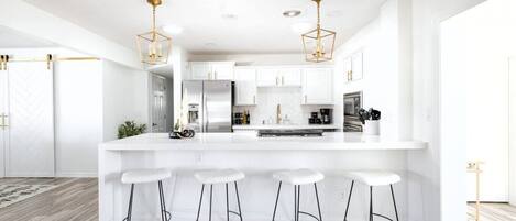 A modern kitchen with white cabinetry, a central island with stools, and pendant lighting.