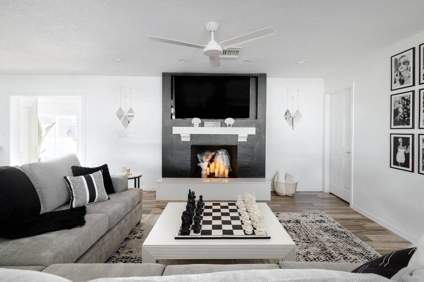 A modern living room with a fireplace, a ceiling fan, and a chessboard on a coffee table.