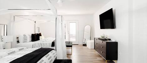 A modern bedroom with a bed, bedside table, dresser, and a TV on the wall.