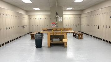 A locker room with a wooden workbench, trash bin, and a sign indicating surveillance.