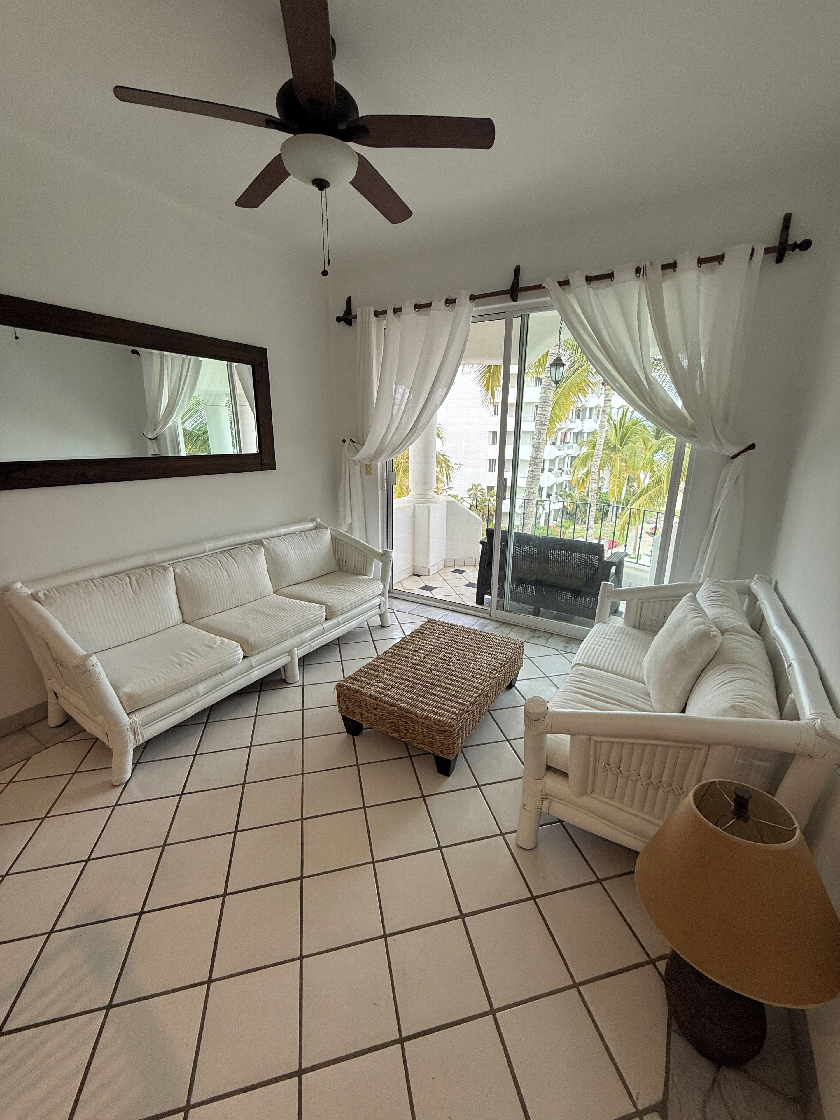A spacious living room with a white sofa, a wicker ottoman, and a floor lamp.