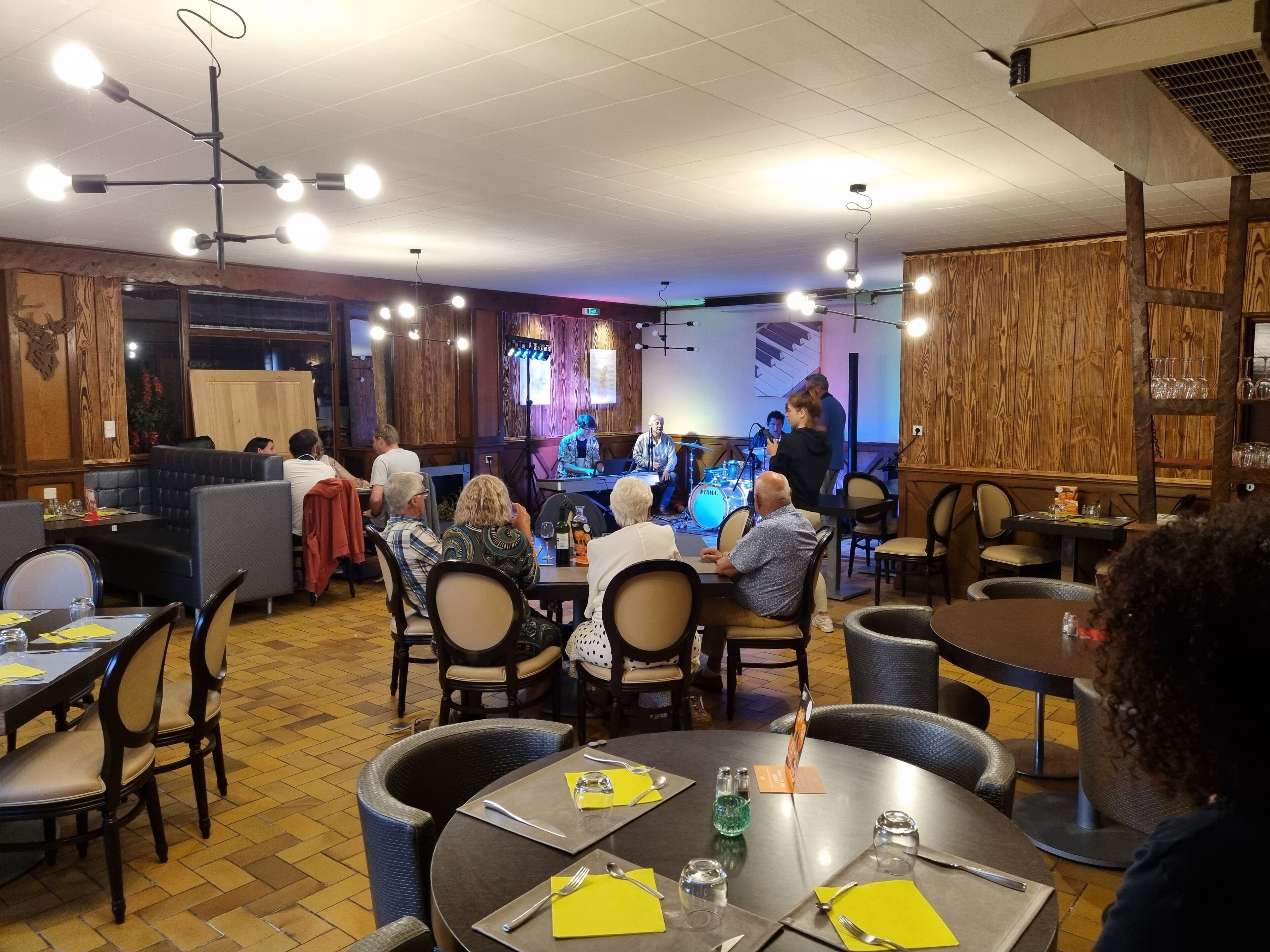 En restaurang med träpanel på väggarna, runda bord och en scen för liveframträdanden.