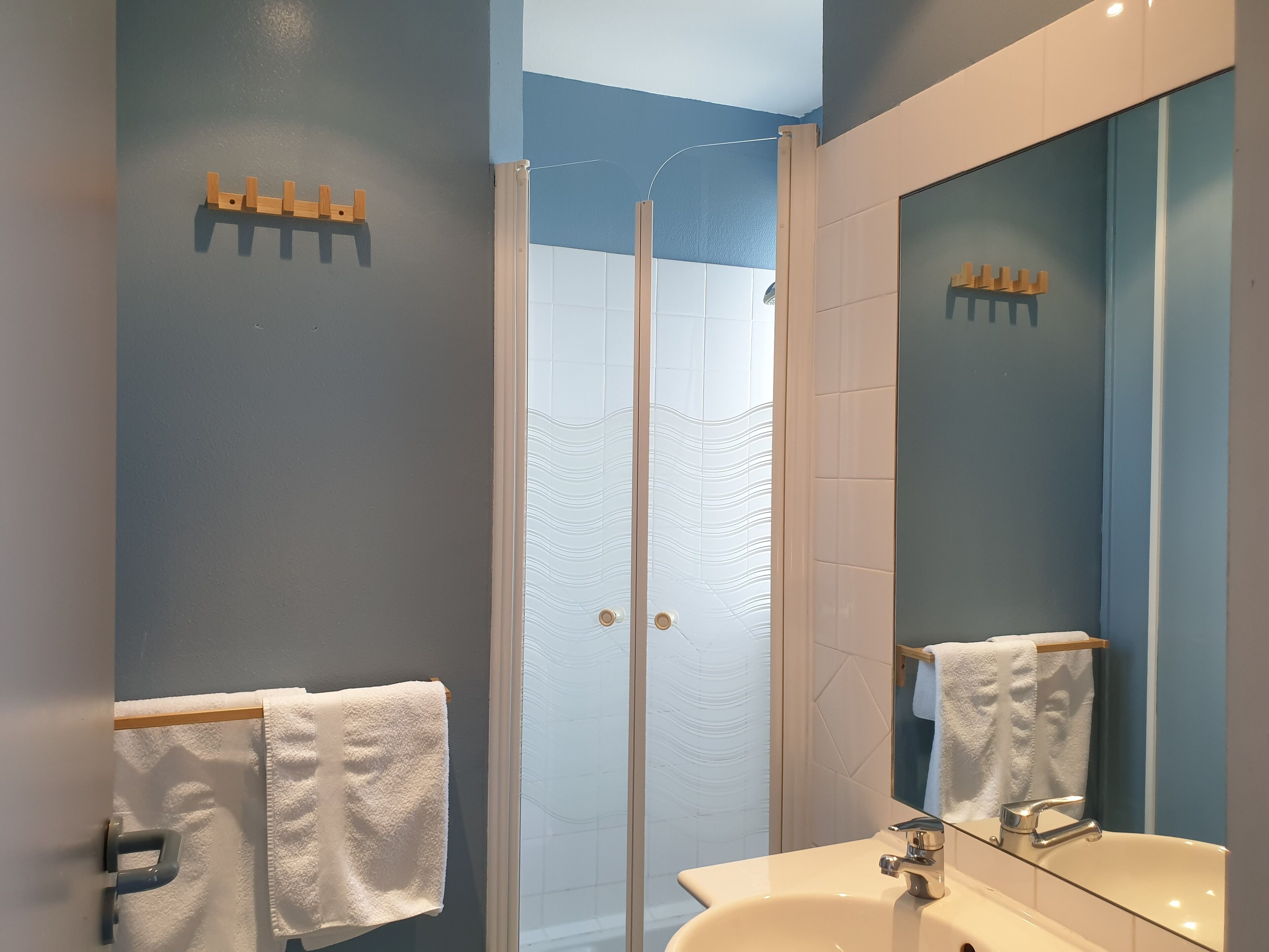 Ein modernes Badezimmer mit Duschabtrennung aus Glas, einem Waschbecken mit Spiegel und zwei Handtüchern an Haken.
