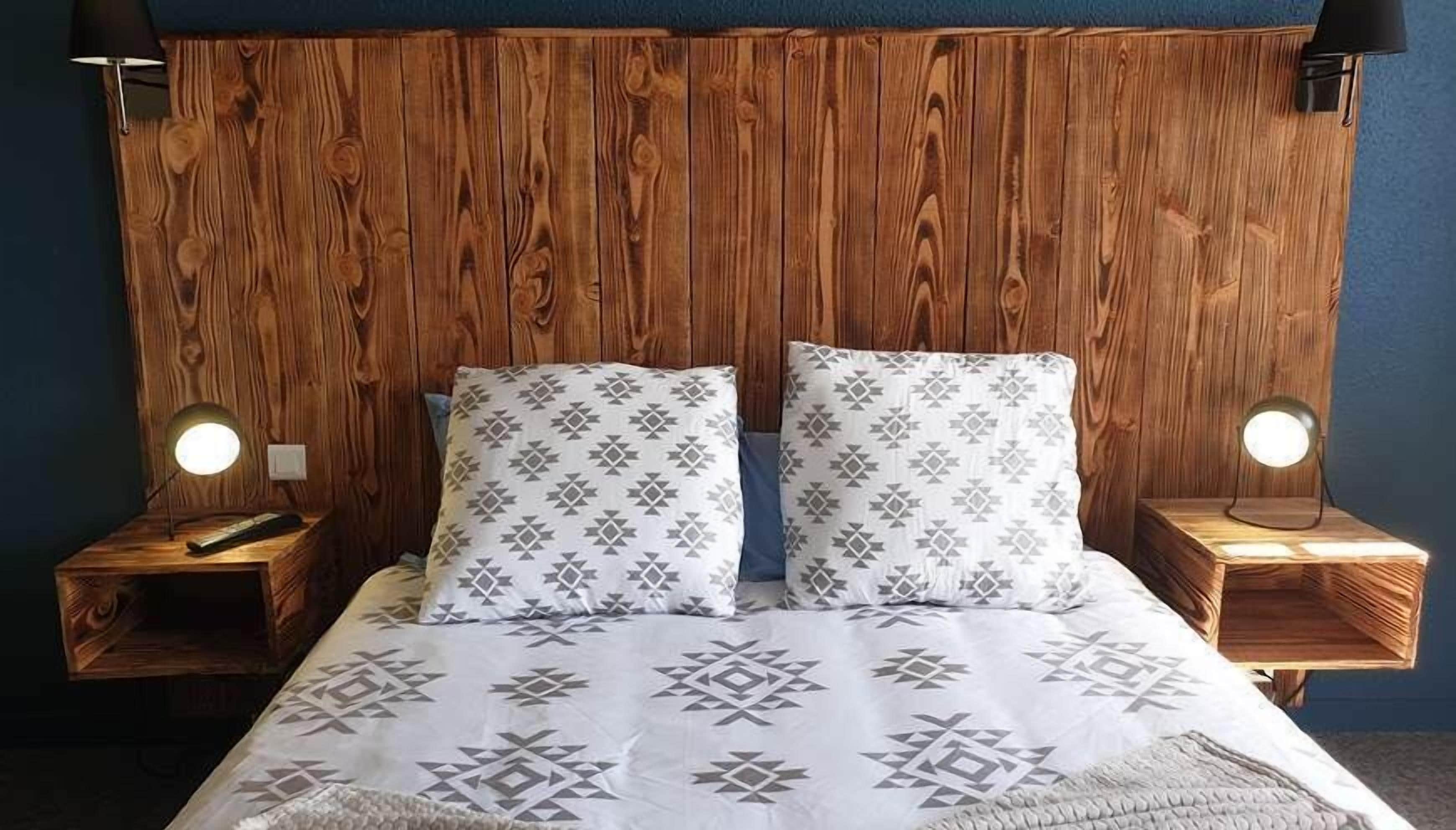 A bed with a geometric patterned bedspread, two pillows, and two bedside lamps.