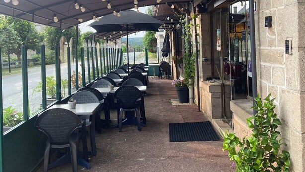 An outdoor patio with tables and chairs, a covered area with hanging lights, and a view of the street. - Auberge Bois de étang Motel les Tilleuls (Peyrat-le-Château)