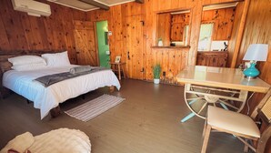 Una habitación de cabaña de madera con una cama, una mesa, sillas, una lámpara y una planta pequeña.