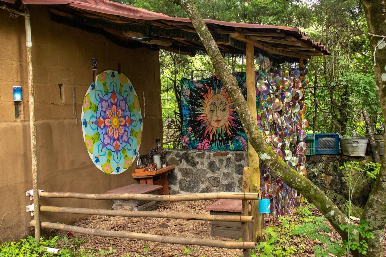 A rustic hut with a colorful circular wall art, a stone wall, and a wooden bench.