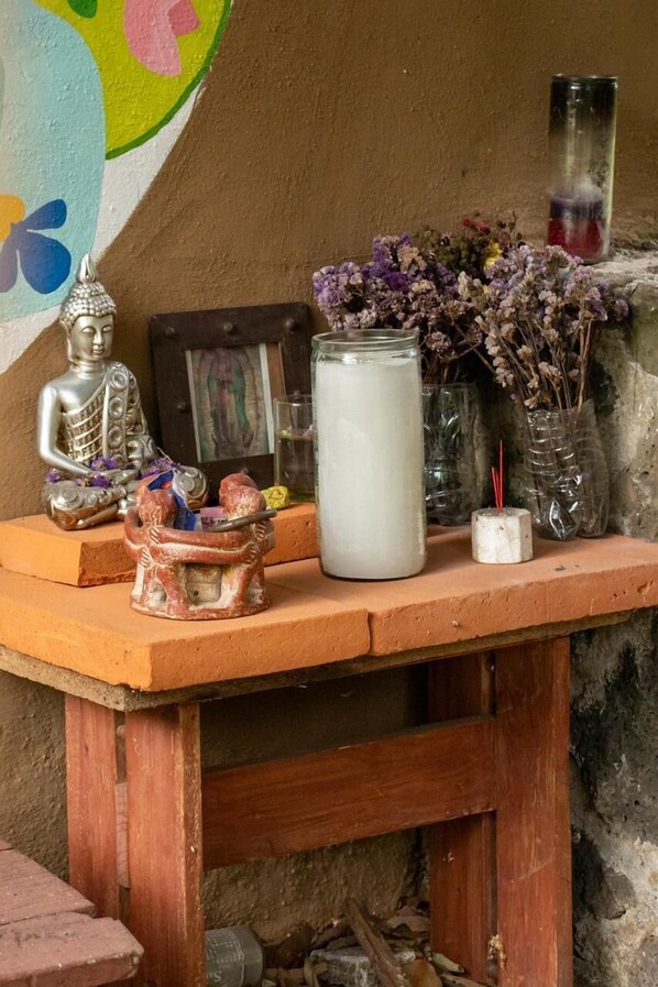 A wooden table with a Buddha statue, a small figurine, a candle, and a glass jar with dried flowers.