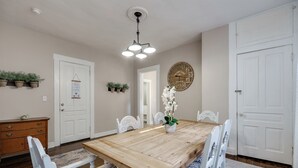A dining room with a wooden table, white chairs, a chandelier, and potted plants.