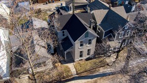 An aerial view of a residential area with multiple houses, including a prominent house with a dark roof and white trim, surrounded by leafless trees and a clear sky. - Downtown Private Studio w/ Kitchenette-near UD (Dayton)
