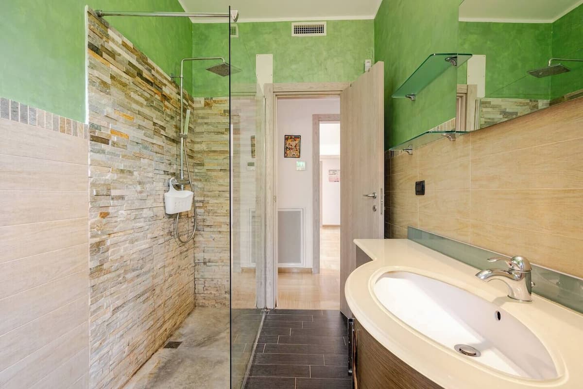 A bathroom with a stone wall, a glass shower enclosure, a sink with a mirror, and a door leading to another room.