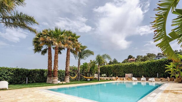 A swimming pool with palm trees, lounge chairs, and a hedge in the background. - Massaroom (Conversano)
