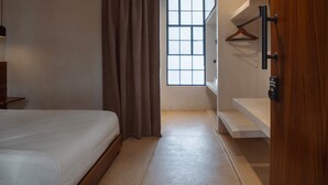 Une chambre à coucher avec un lit, une fenêtre, une porte en bois et un porte-manteau fixé au mur.