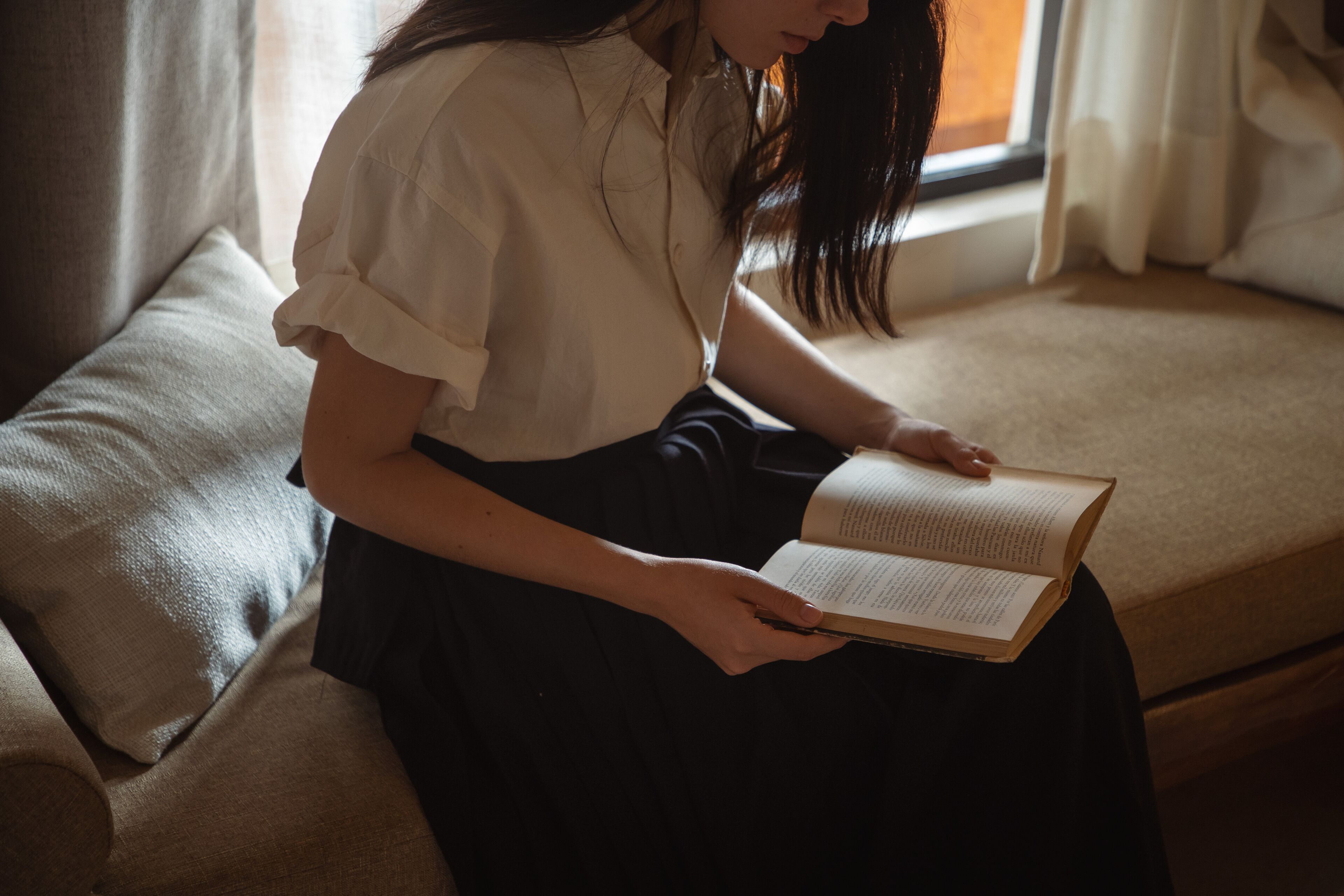 Une personne assise sur un canapé, en train de lire un livre.