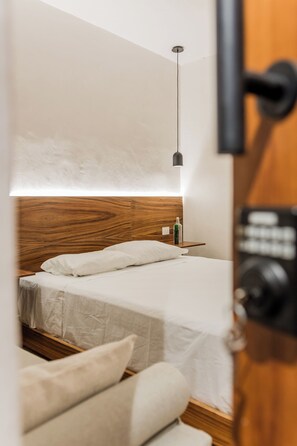 A bedroom with a wooden headboard, a bed with white bedding, a bedside table with a bottle, and a hanging light fixture. - Mamacha's Residence Private Apt  (Valladolid)