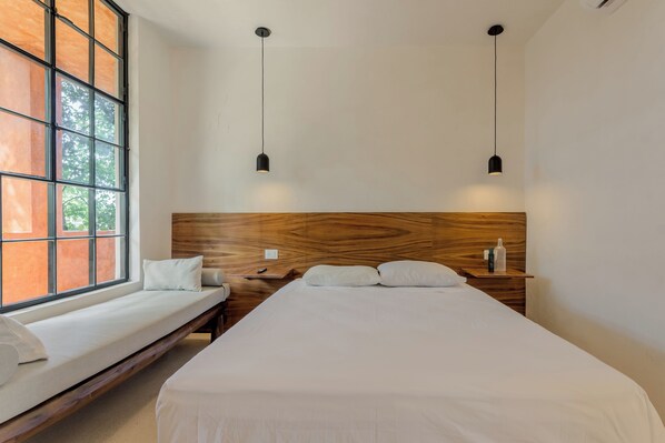 A modern bedroom with a large window, a wooden headboard, two bedside tables, and a bed with white linens. - Mamacha's Residence Private Apt  (Valladolid)