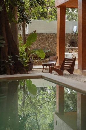 A pool area with wooden chairs and a stone wall. - Mamacha's Residence Private Apt  (Valladolid)