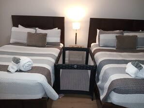 A hotel room with two beds, each with striped bedding and pillows, a small table, and a nightstand with a lamp.