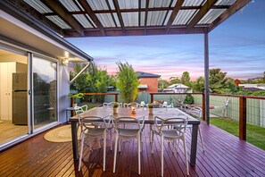 An outdoor patio with a wooden deck, a table with chairs, and a glass door leading to a modern kitchen. - Kookaburra Krib! Walk 2 Little Beach & Shoal Bay (Nelson Bay)
