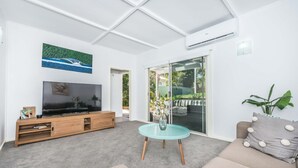 Ein modernes Wohnzimmer mit Flachbildfernseher, Glastisch und einer Couch mit dekorativen Kissen.