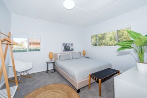 A modern bedroom with a bed, bedside tables, a chair, a hanging rack, and a large window with a view of greenery. - Kookaburra Krib! Walk 2 Little Beach & Shoal Bay (Nelson Bay)