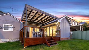 Ein Haus mit überdachter Terrasse, einer Holzterrasse und einem Rasenstück.