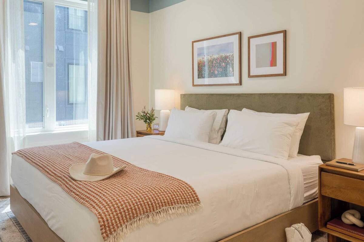 Une chambre d’hôtel avec un grand lit, une table de chevet avec une lampe et une fenêtre avec des rideaux.