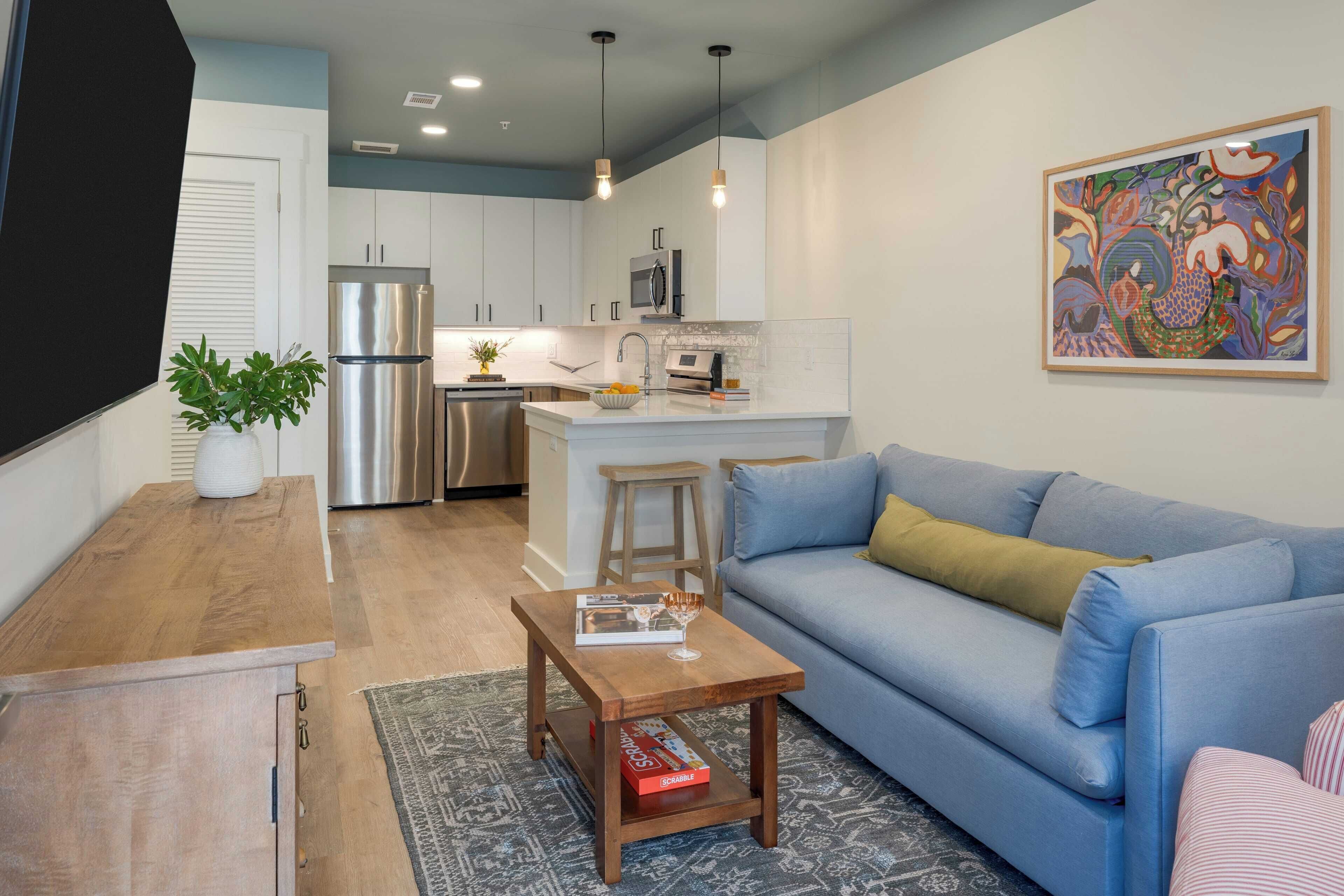A modern kitchen with stainless steel appliances, a central island, and a dining area with a blue sofa and a coffee table.