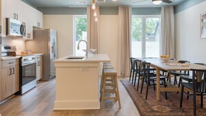 Una cocina moderna con una isla central, electrodomésticos de acero inoxidable y un comedor con mesa y sillas de madera.