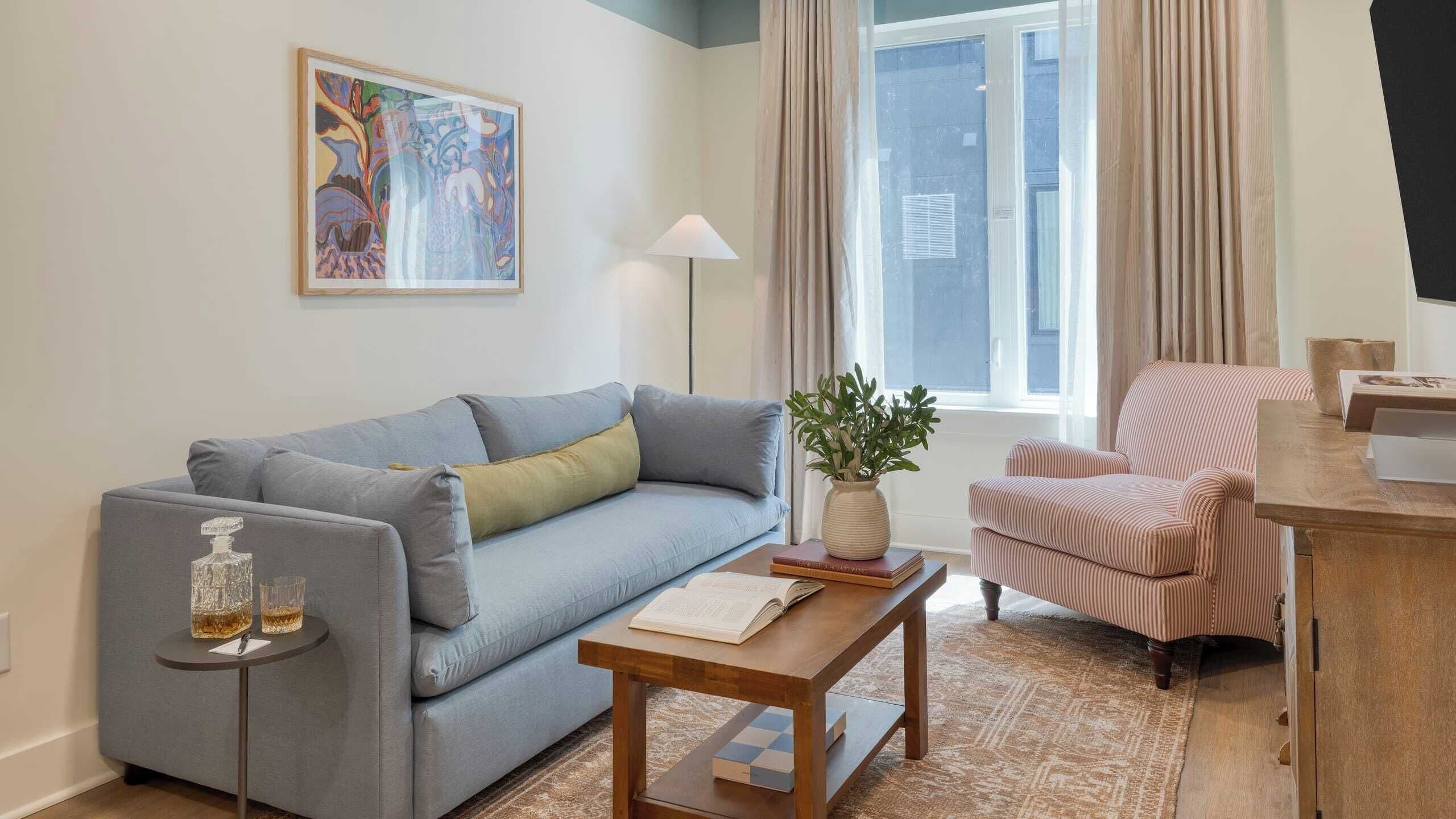 Una sala de estar con un sofá gris, un sillón a rayas, una mesa de centro de madera y un cuadro en la pared.