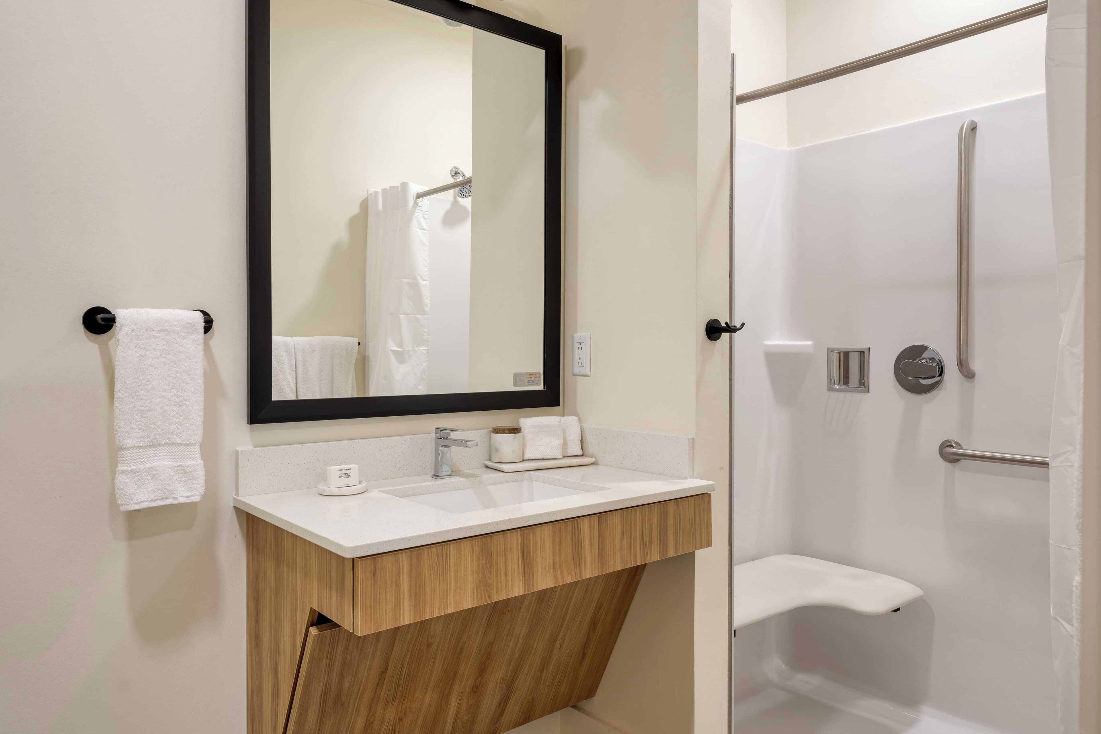 A modern bathroom with a white sink, wooden vanity, a large mirror, and a walk-in shower.