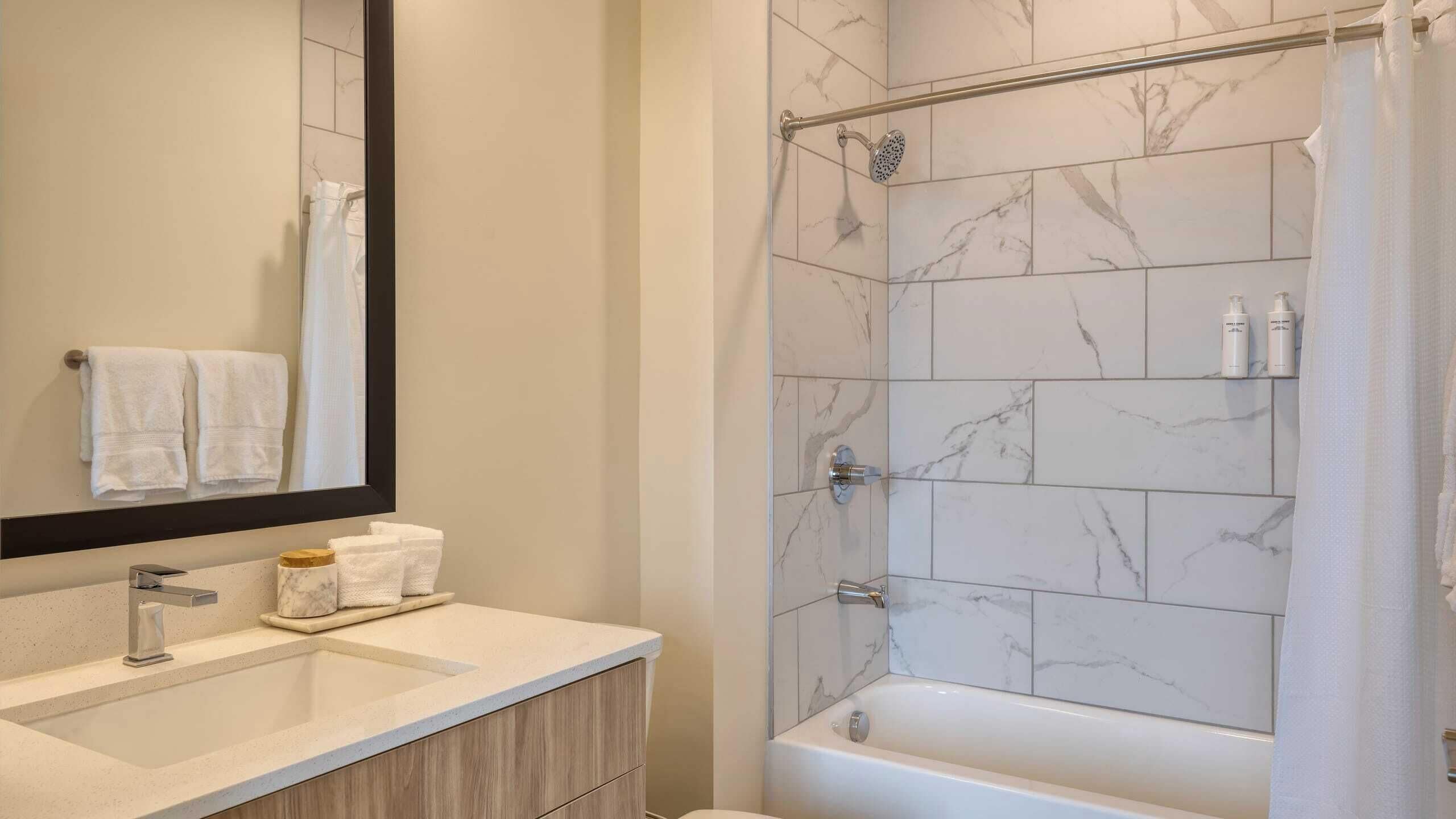 A bathroom with a marble shower, a bathtub, a sink with a mirror, and two towels hanging on the wall.