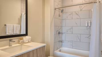 A bathroom with a marble shower, a bathtub, a sink with a mirror, and two towels hanging on the wall.