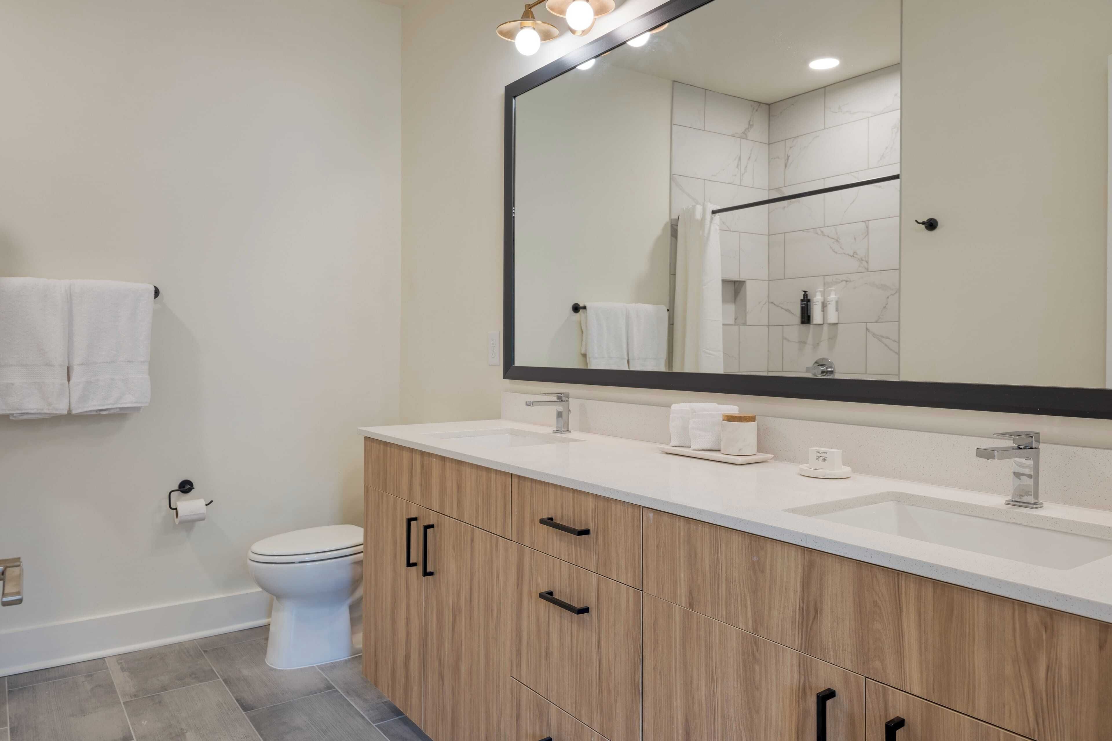 Un baño moderno con un espejo grande, dos lavamanos y armarios de madera.