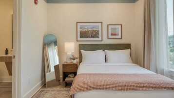 Una habitación de hotel con una cama, una mesita de noche, un espejo y dos cuadros en la pared.