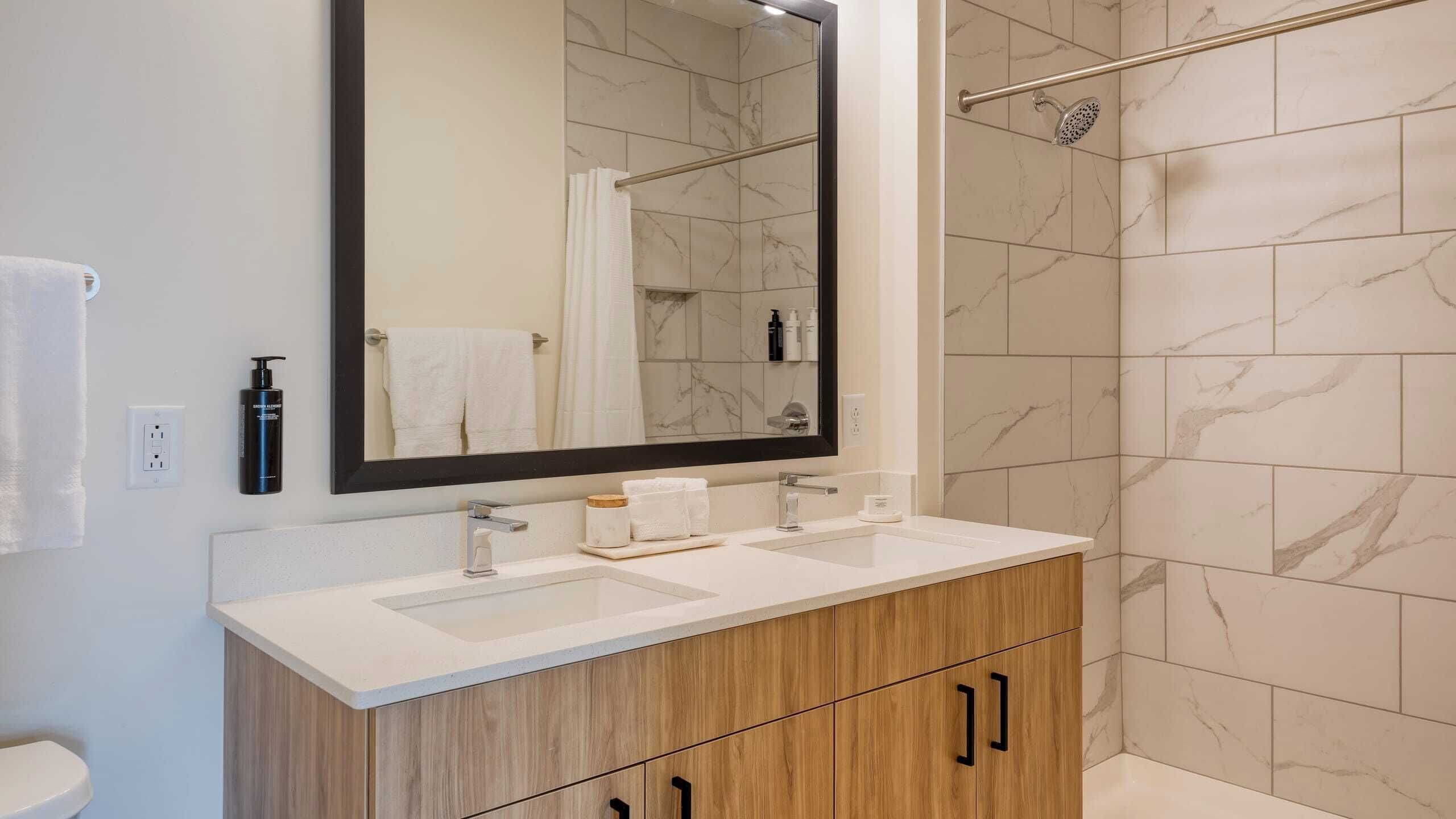 A bathroom with a double sink vanity, a large mirror, and a shower area with a glass door.