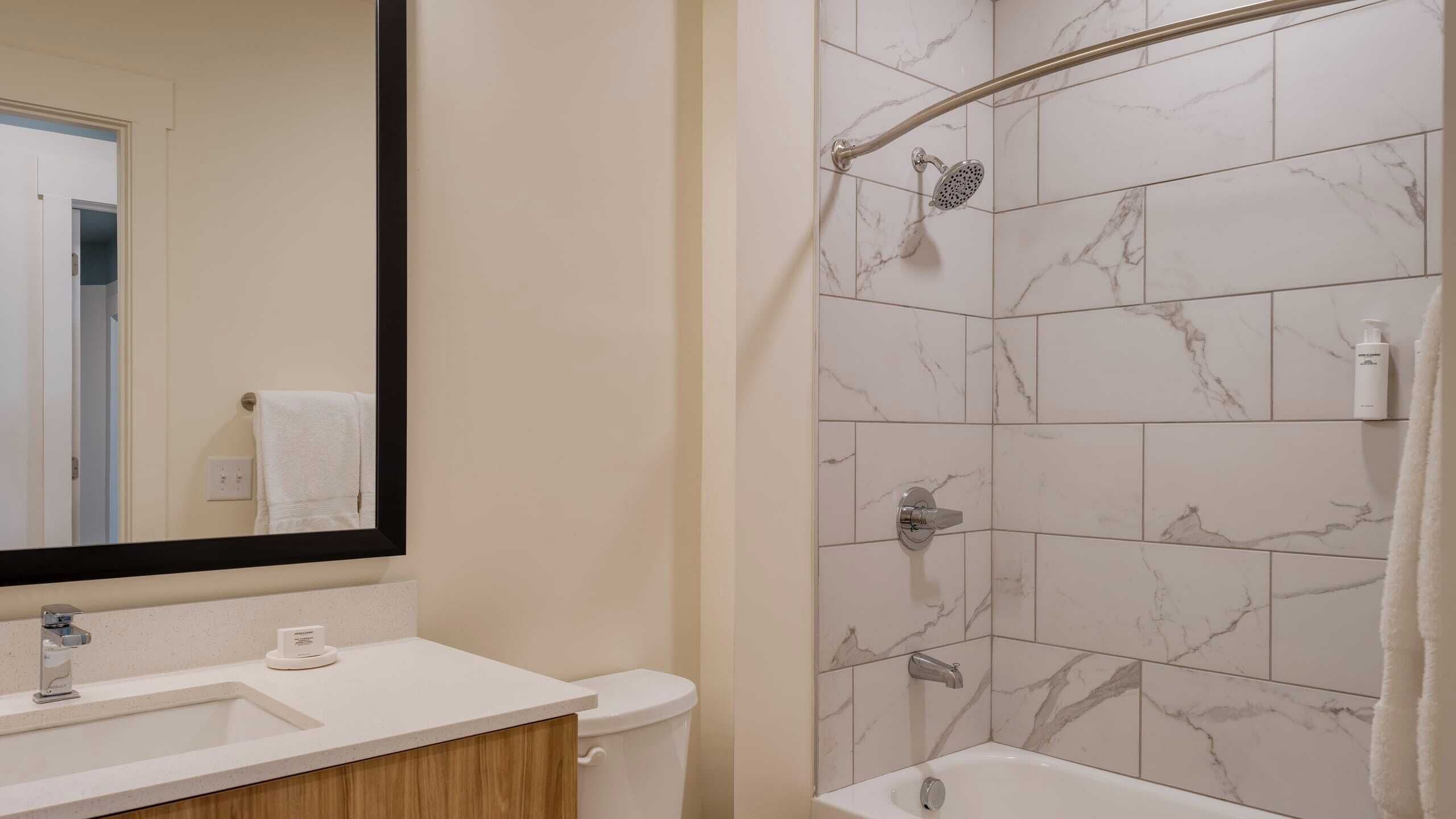 A bathroom with a shower, toilet, sink, and a large mirror.