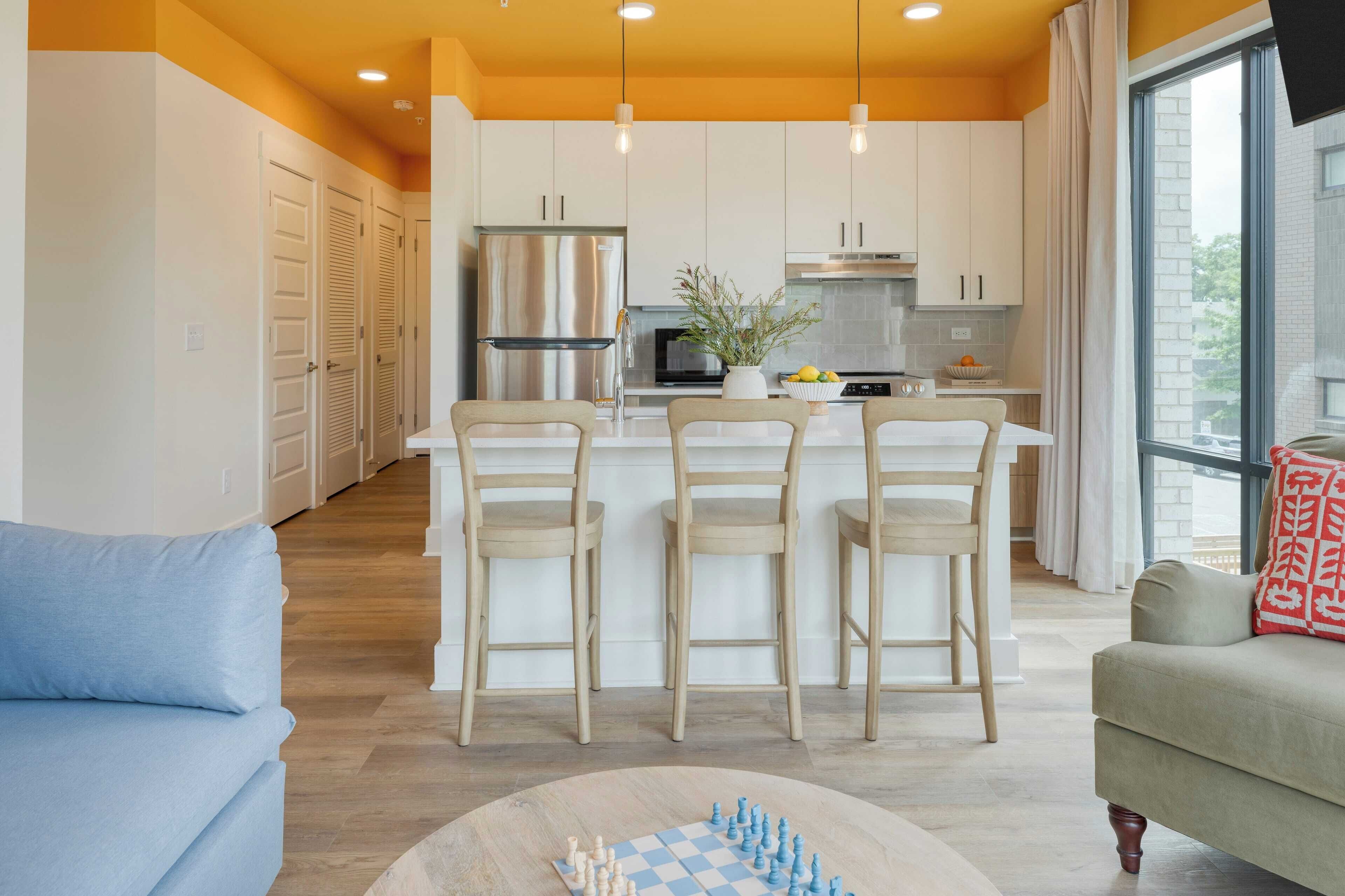 Una cocina moderna con una isla central, taburetes de bar y un comedor con un tablero de ajedrez.