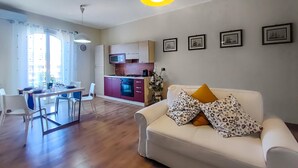 Una sala de estar moderna con sofá, una mesa de comedor con sillas, una zona de cocina y un ventanal con cortinas.