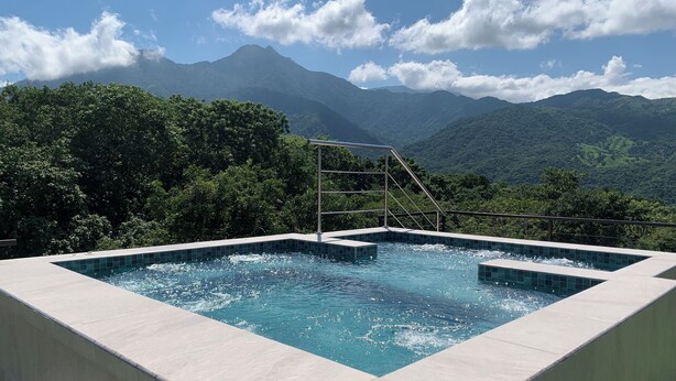A rectangular pool with a metal ladder, surrounded by a concrete deck, set against a backdrop of lush green mountains and a clear sky. - Alto Casa de Montaña (Santa Marta)