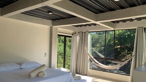 A bedroom with a large bed, a hammock, and a view of trees through a large window. - Alto Casa de Montaña (Santa Marta)