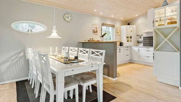 A modern kitchen with white cabinetry, a dining area with white chairs, a clock on the wall, and a window with a view of trees. - Amazing home in Højslev with sauna (Højslev)