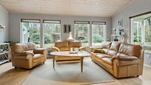A spacious living room with leather sofas, a glass coffee table, and large windows offering a view of the outdoors. - Amazing home in Højslev with sauna (Højslev)