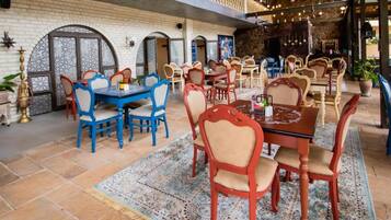 Een restaurant met meerdere eettafels en stoelen, een kamerkleed met patroon en een bakstenen muur.