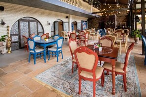 Un restaurant doté de plusieurs tables et chaises, d’un tapis à motifs et d’un mur en briques.