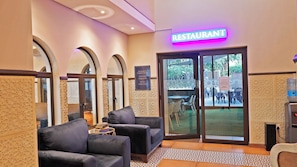 A restaurant with a neon sign, seating area with chairs, a water dispenser, and a patterned floor.