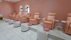 A row of massage chairs with footrests and small tables, arranged in a room with pink walls and large windows. - Qurtuba Resort And Events (Johannesburg)