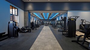 Une salle de sport équipée de divers appareils d’exercice, dotée d’un couloir central et d’un plafond éclairé de lumières bleues.