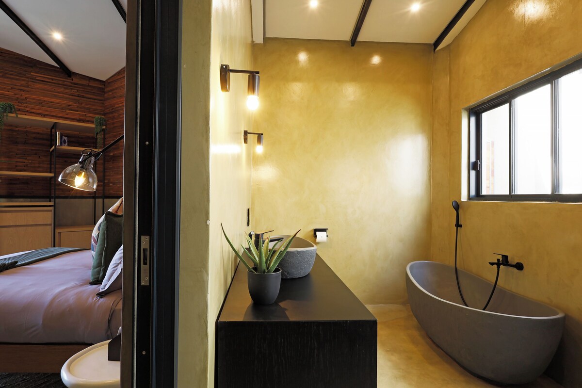 A modern bathroom with a freestanding bathtub, a large mirror, and a potted plant.