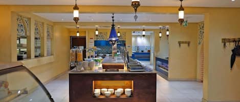 A hotel lobby with a central reception desk, decorative wall patterns, and a tiled floor.